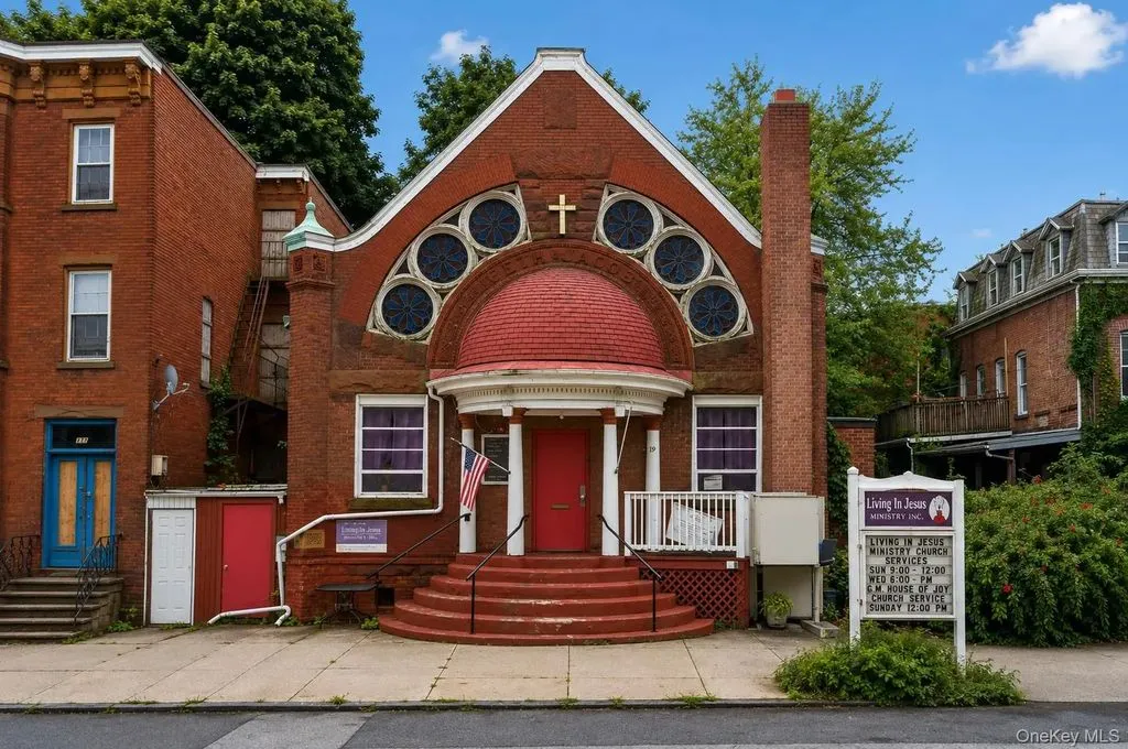 Red-brick church front with round stained-glass windows and a red door